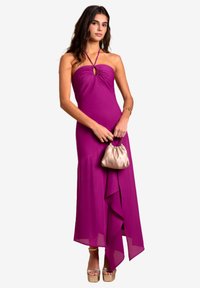 Paarse jurk tot op de vloer met een halternek en keyhole-detail. Kenmerkt zich door een gedrapeerde rok en een beige clutch tas. Gladde stofstructuur.