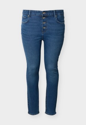 Blå slim-fit denimjeans med fire synlige forreste knapper, forlommer og bæltestropper mod en lys baggrund.