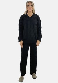 Schwarzer Strickpullover mit Zopfmuster und passende Hose, mit V-Ausschnitt, langen Ärmeln und lockerer Passform. Der Stoff wirkt weich mit einem strukturierten Muster.