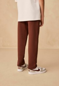 Brązowe dresy o miękkiej fakturze, w połączeniu z białymi i brązowymi sneakersami Nike z wyraźnym logo i eleganckim designem.