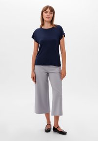 Námořnická modrá top s krátkým rukávem spárovaný s světlými šedými kalhotami s širokými nohavicemi a černými plochými botami. Hladká textura, uvolněný střih a univerzální design.