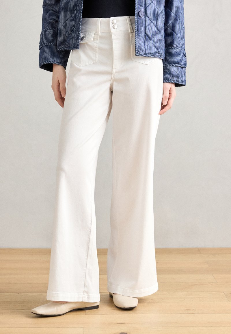 White, wide-leg trousers feature a high waist, two front pockets, and subtle button accents. The fabric appears smooth and textured.