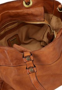 Braune Leder-Tote-Bag mit weicher Textur, versehen mit zwei Knopfakzenten und einer Reißverschlusstasche im Inneren, ergänzt durch ein beiges Innenfutter.
