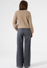 Un pull en beige duveteux à manches longues associé à un jean en denim sombre à taille haute et jambes larges, comportant des poches arrière et des coutures discrètes.