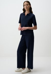 Marineblauw two-piece outfit met een kort mouwtop met kraag en wijde broek, voorzien van verticale geribbelde textuur en gecombineerd met witte sneakers.