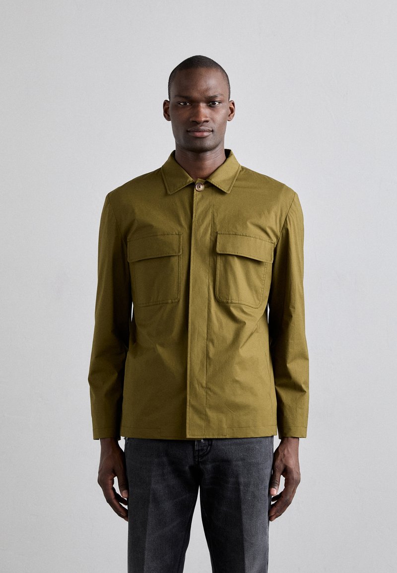 Oliven grøn jakke med spidse kraver, to brystlommer og forreste knaplukning. Glat tekstur, lange ærmer, tætsiddende pasform.