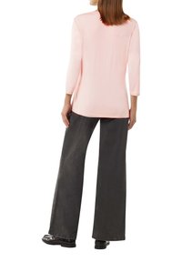 Light pink long-sleeve top with a rounded neckline, paired with wide-leg dark gray jeans. Smooth fabric with minimal stitching details.