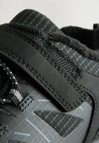 Black athletic shoe with textured synthetic upper, elastic laces, Velcro strap, and reflective accents on a smooth dark sole.