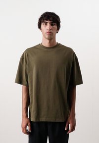 Oliven grøn oversized bomulds T-shirt med rund halsudskæring og korte ærmer, der har en afslappet pasform og glat tekstur.