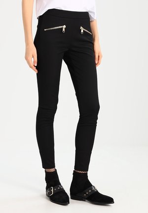 Pantalons noirs ajustés avec deux poches avant zippées, conçus en tissu extensible. Accentué par des zips dorés, avec une taille haute.