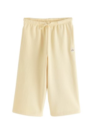 Short beige clair jusqu'au genou avec taille élastique, cordon de serrage et un petit patch arc-en-ciel sur le côté droit.