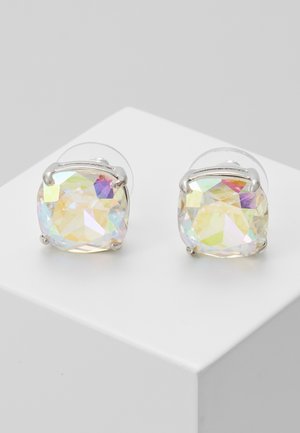 Okrągłe, opalizujące kolczyki z kryształami osadzone w srebrnych lokujących oprawkach, prezentowane na białej podstawce na szarym tle.