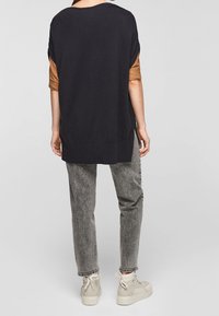 Överdimensionerad svart sweatshirt med rullade ärmar, i kombination med grå strukturerade byxor och beige högstövlar, sedd bakifrån.