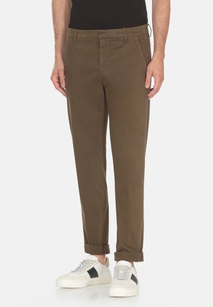 Chino in cotone marrone con vestibilità slim, tasche laterali e orli arrotolati, abbinati a sneaker bianche con accenti neri.