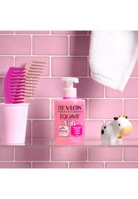 Revlon Equave Kids rosa balsamerende sjampo i en klar flaske, sammen med en rosa kam og et hvitt håndkle, på en rosa flislagt hylle.