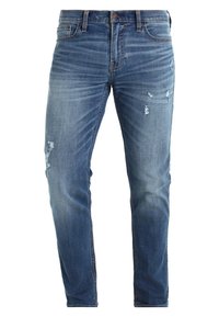 Blå denimjeans med slim fit, som har blekta områden och flera slitna lappar framtill för en använd look.