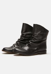 Botas de cuero negras hasta el tobillo con un diseño holgado, puntera redonda, tacón bajo y un sutil logo de mariposa en el lado exterior. Textura suave.