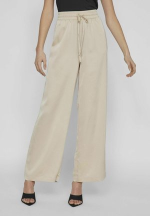 Beige weit geschnittene Hose mit elastischem Bund und Kordelzug, aus glattem Stoff gefertigt. Mit minimalistischer Gestaltung und seitlichen Taschen akzentuiert.