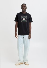 Svart bomulls T-skjorte med grafisk trykk som har "KEEP IT SIMPLE" og "SLOW DOWN" i grønn og rosa, kombinert med lyseblå, løstsittende jeans.