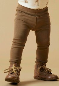 Bruine legging met ribbelstructuur en een aansluitende pasvorm, gecombineerd met bruine leren enkellaarsjes met decoratieve stiksels en veters.