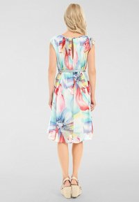 Blommönstrad klänning med korta ärmar, cinchad midja och knälång nederdel. Har ett färgglatt mönster med lätt, flödande tyg och en knytdetalj.