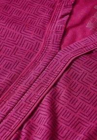 Fuchsia-Stoff mit einem geometrischen Muster aus schwarzen Linien. Er hat einen Reißverschluss und strukturierte Akzente entlang der Nähte.