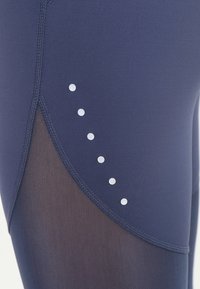 Marina blå träningsleggings med meshnäst, med sex runda vita accentprickar längs sömmen. Slät, töjbar tyg.