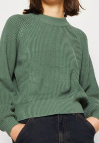 Maglione verde a coste con scollatura a girocollo e maniche raglan, caratterizzato da un tessuto testurizzato e una vestibilità rilassata.