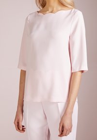 Ljusrosa blus med scallopad halsringning, trekvartsärmar och mjukt tyg. Designad med en avslappnad passform och minimalistisk stil.