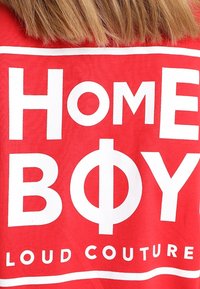 Camiseta de algodón roja con el texto en blanco "HOME BOY" en la parte superior de la frase "LOUD COUTURE". Diseño simple con letras grandes.