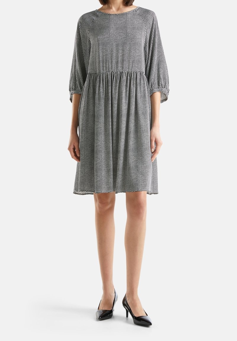 Černobíle vzorované šaty s volným střihem, sukní ke kolenům, 3/4 rukávy a nařaseným pasem, doplněné černými vysokými podpatky.