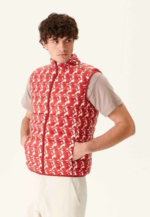 Rode gewatteerde vest met een wit abstract patroon, hoge kraag, volledige voorkleur en zijzakken, gedragen over een beige shirt met korte mouwen.