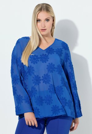 Blå gennemsigtig bluse med lange ærmer, V-hals og indviklet blomsterbroderi. Matcher med blå bukser, der skaber et sammenhængende outfit.