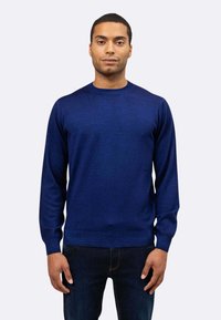 Maglione blu navy con scollo rotondo, maniche lunghe e polsini a costine, realizzato in tessuto morbido, indossato sopra jeans scuri.