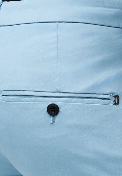 Κοντινό πλάνο ανοιχτό μπλε παντελονιού που δείχνει την πίσω τσέπη με μαύρο κουμπί και μικρή μεταλλική λεπτομέρεια λογότυπου στην άκρη της τσέπης.