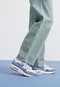 Nike Air Max 1 sneakers i lys blå og grå, med mesh og semsket lærmaterialer, avrundet form og synlig luftdemping i sålen.