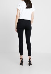 Černé úzké džíny se středním pasem a hladkou texturou, kombinované s bílým tričkem s vyhrnutými rukávy a černými lodičkami na vysokém podpatku.