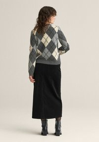 Harmaa ja kerma argyle-neule pyöreällä pääntiellä, yhdistetty mustaan farkkuhameeseen ja nilkkureihin, nähtynä takaa.