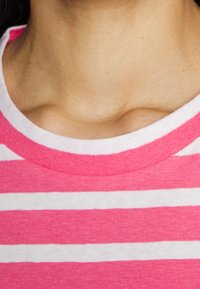 Detailní záběr na krk a horní část hrudníku osoby, která má na sobě růžové a bílé vodorovně pruhované tričko s kulatým výstřihem.