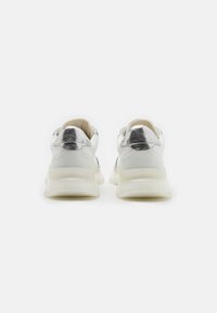 Zapatillas blancas con un detalle brillante en el talón en color plata. Parte superior de cuero liso, suela blanca gruesa y diseño minimalista sin patrones visibles.