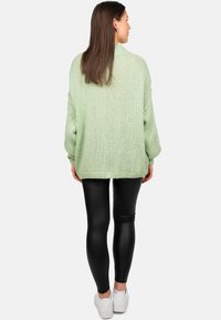 Maglione lavorato a maglia verde chiaro con vestibilità ampia, texture a costine e spalle scese, abbinato a leggings neri e sneakers bianche.