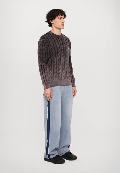Pull en maille torsadée gris foncé avec des poignets côtelés, associé à un jean taille haute bleu clair à jambes larges avec une rayure sur le côté navy et des chaussures noires.