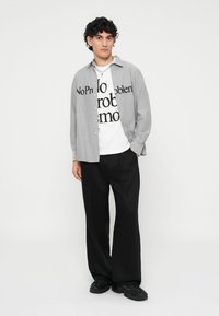 Gray button-up shirt layered over a white t-shirt with black text, paired with loose black pants and black sneakers. Simple design and fit.
