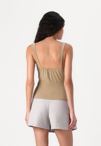 Beige tettskjorte med brede stropper og samlet bak, kombinert med lysegrå shorts. Myk tekstur og enkelt design.