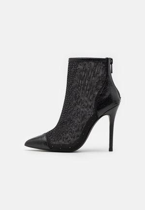 Černá kotníková bota s špičatou špičkou, průhledným síťovaným svrškem s texturovanými detaily a lesklým černým lakovaným podpatkem. Zapínání na zip vzadu.