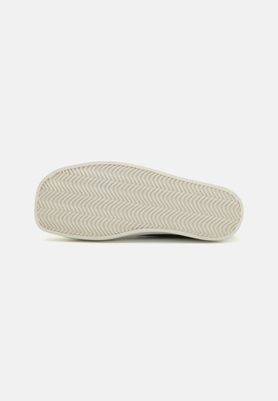 White rubber sole with a zigzag texture and smooth edges. Circular toe cap and flat, even surface, designed for traction and stability.