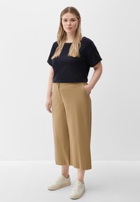 Black, short-sleeve top with rolled cuffs, paired with tan wide-leg trousers featuring side pockets. Model wears cream sneakers.