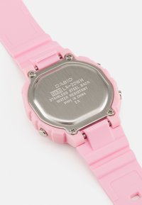 La montre Casio LA-20WH présente un bracelet en caoutchouc rose, un fond en acier inoxydable et un boîtier rectangulaire avec une surface texturée. Résistante à l'eau.