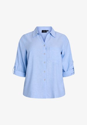 Gaiši zilā krāsā, īsām piedurknēm, pogājamais krekls ar apkakli, vienu krūšu kabatu un ruļļpiedurkņu iespējām. Izgatavots no strukturētas auduma.