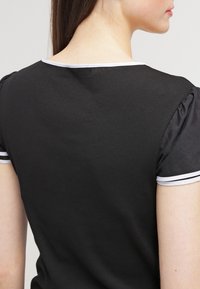 Woman wearing a black ribbed short-sleeve shirt with white trim on the neckline and sleeve cuffs, shown from the back and side profile.